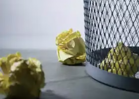 Close-up of crumpled yellow paper around a mesh trash bin, symbolizing rejected ideas or recycling.