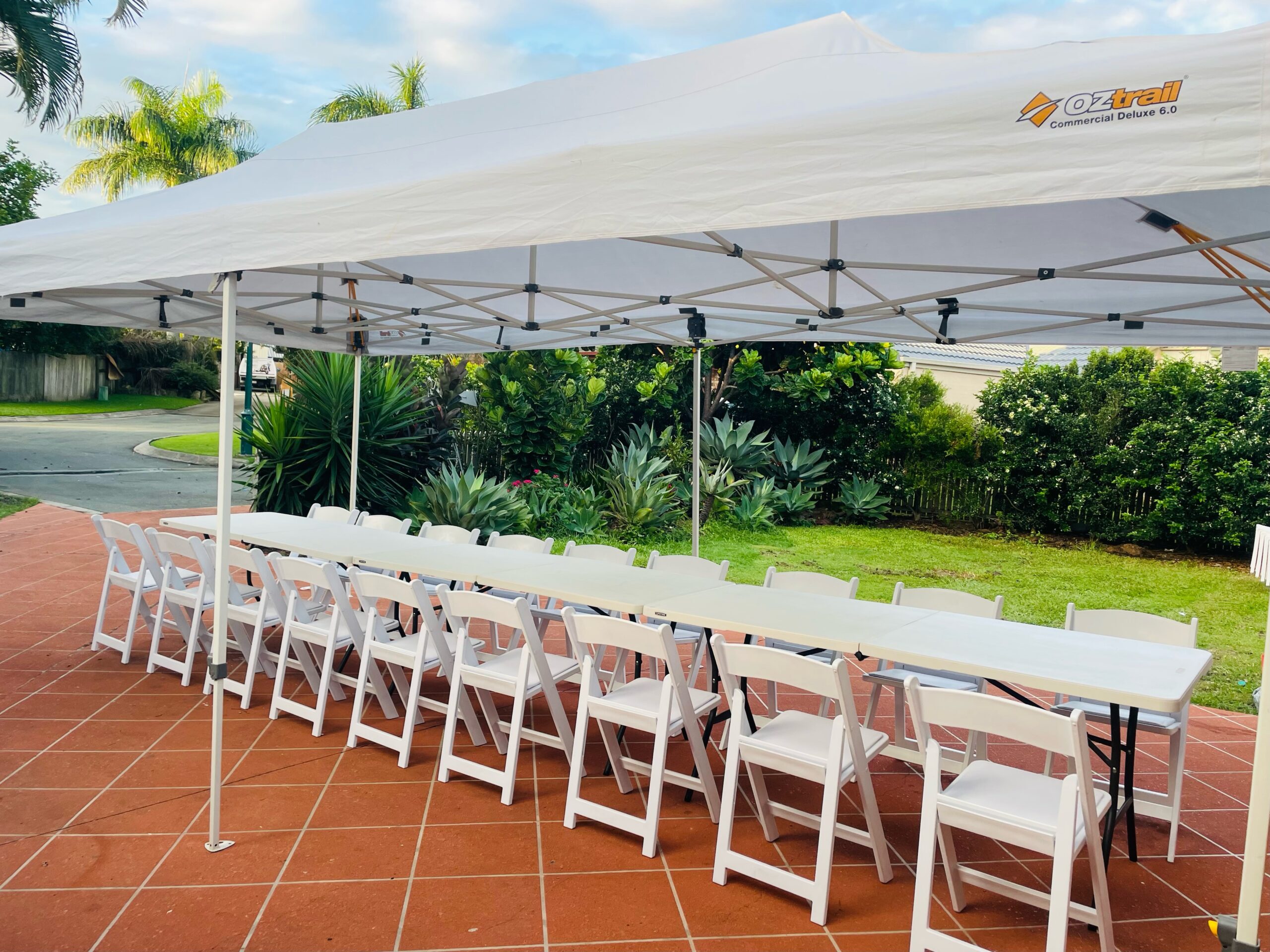Gazebo with long tables and white chairs set up for a backyard party