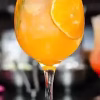 Refreshing orange cocktail with ice, garnished with rosemary and orange slice. Perfect for summer parties.