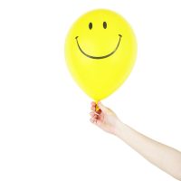 Bright yellow balloon with a smiley face held in a hand on a white background.